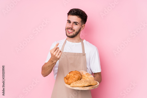 Young caucasian baker man isolated pointing with finger at you as if inviting come closer.
