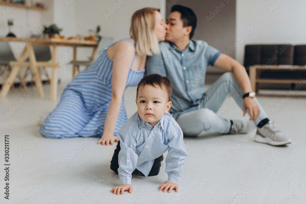 Happy multicultural family having fun together in the kitchen. Asian dad and caucasian mom teach son to crawl Happy multicultural family having fun together in the kitchen. Asian dad and caucasian mom teach son to crawl