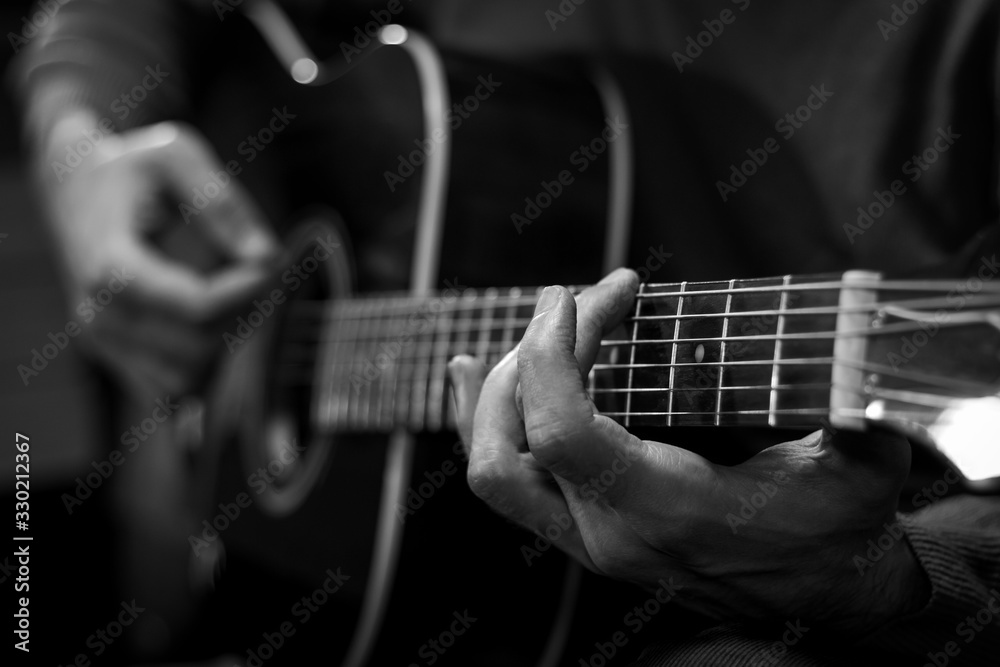 Close up view of hands playing acoustic western guitar. Black and white image.