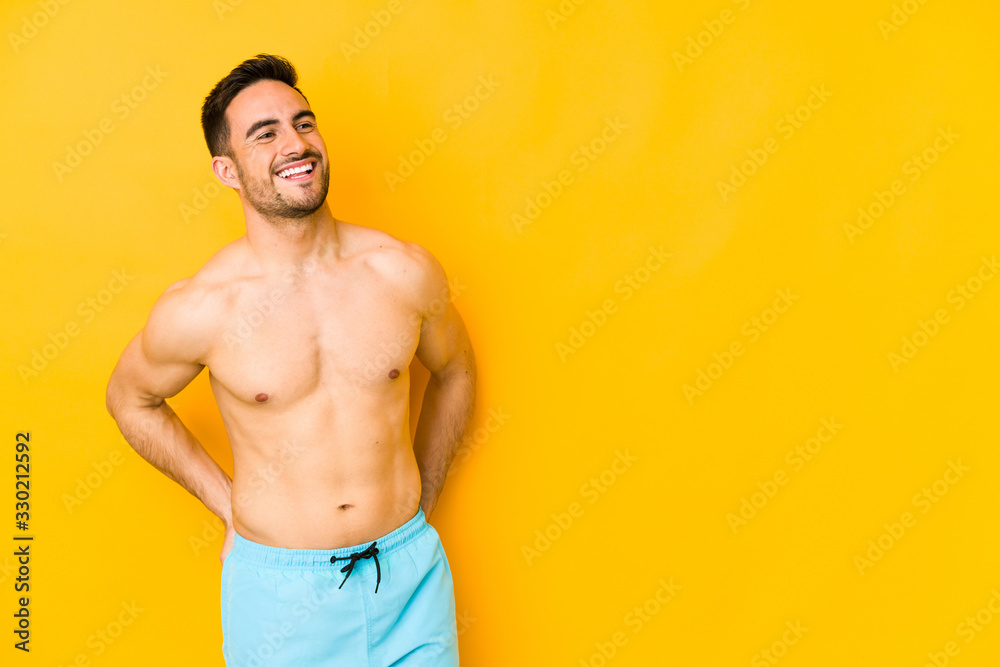 Young caucasian man with swimsuit isolated on yellow background Young caucasian man with trrelaxed and happy laughing, neck stretched showing teeth.