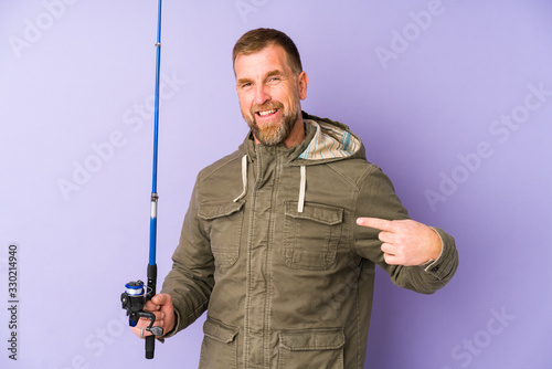 Senior fisherman isolated on purple background person pointing by hand to a shirt copy space, proud and confident