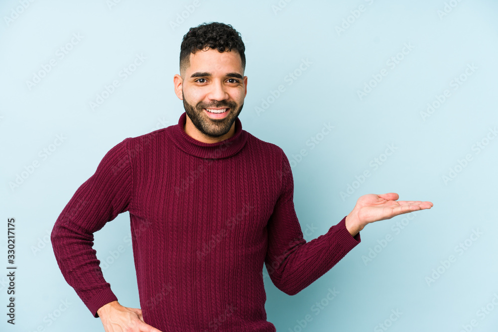 Young mixed race arabic man isolated showing a copy space on a palm and holding another hand on waist. Young mixed race arabic man isolated showing a copy space on a palm and holding another hand on waist.