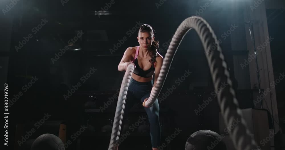 Active motivated female athlete training in gym, having a crossfit session with battle ropes, achieving goals enjoying healthy lifestyle 4k footage
