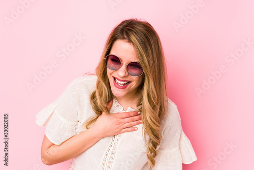 Young caucian woman with glasses isolated on pink background laughs out loudly keeping hand on chest. © Asier