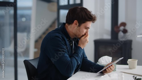 Sick business man getting flu in office. Ill man sneezing near laptop indoor.
