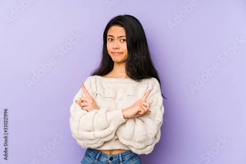 Young chinese woman isolated on a purple background points sideways, is trying to choose between two options.