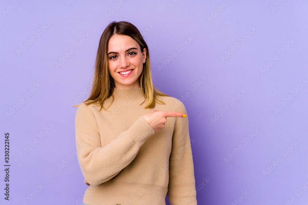 Young caucasian woman isolated on purple background smiling and pointing aside, showing something at blank space.