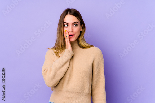 Young caucasian woman isolated on purple background is saying a secret hot braking news and looking aside