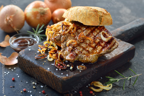 Gegrilltes Lendensteak vom Rind mit Röstzwiebeln im reschen Brötchen serviert - Big meat sandwich with a grilled beef steak and fried onion rings on a fresh roll photo