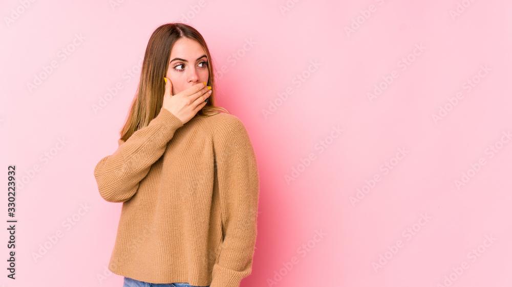 Young caucasian woman isolated on pink background thoughtful looking to a copy space covering mouth with hand.