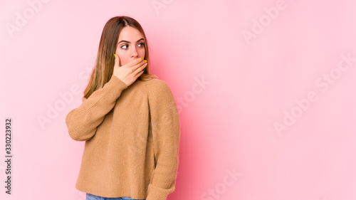 Young caucasian woman isolated on pink background thoughtful looking to a copy space covering mouth with hand.