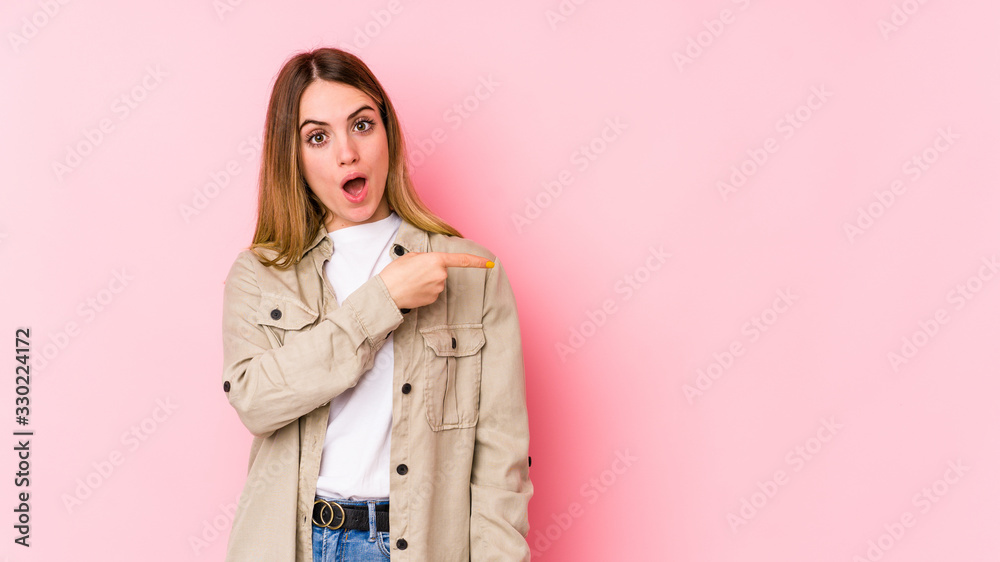Young caucasian woman isolated on pink background smiling and pointing aside, showing something at blank space. Young caucasian woman isolated on pink background smiling and pointing aside, showing something at blank space.