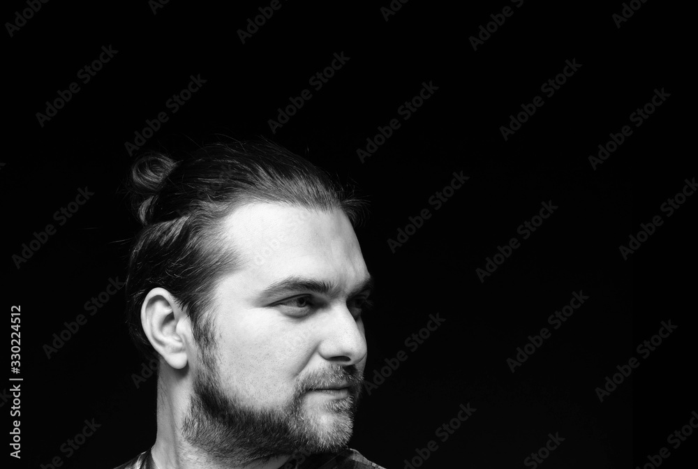 side view of black and white portrait of handsome concentrated man with stylish beard and elegance hair bun looking away isolated on black