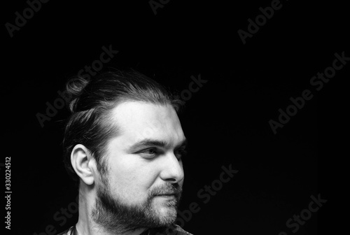 side view of black and white portrait of handsome concentrated man with stylish beard and elegance hair bun looking away isolated on black