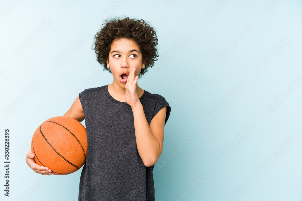 Kid boy playing basketball isolated on blue background is saying a secret hot braking news and looking aside