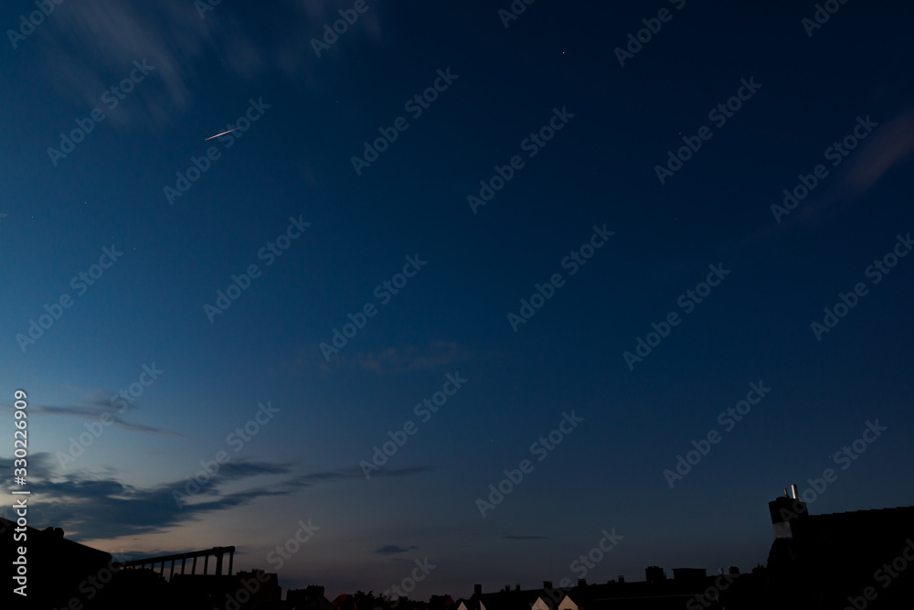 Bright iridium communication satellite flare at sunset above city houses