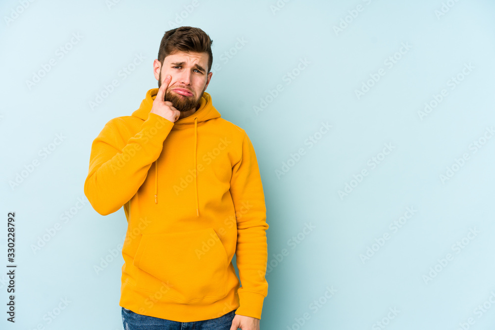 Young caucasian man isolated on blue background crying, unhappy with something, agony and confusion concept. Young caucasian man isolated on blue background crying, unhappy with something, agony and confusion concept.