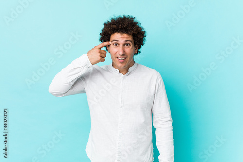 Young curly mature man wearing an elegant shirt showing a disappointment gesture with forefinger.