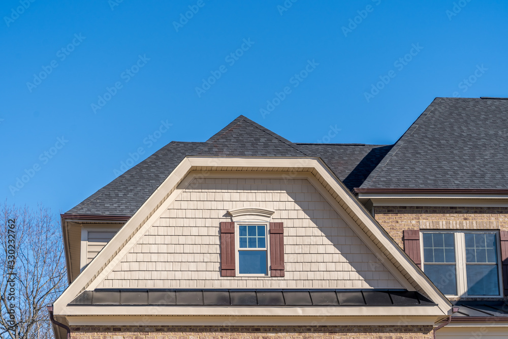 Gable with tan shingle and shake siding, double hung windows with white frame, on a dutch roof attic at an American single family home neighborhood USA