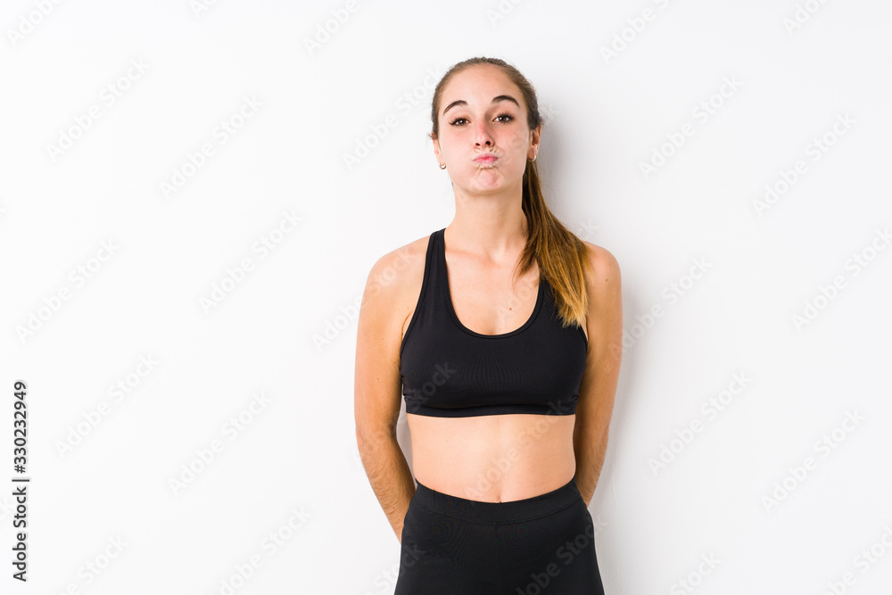 Young caucasian fitness woman posing in a white background blows cheeks, has tired expression. Facial expression concept. Young caucasian fitness woman posing in a white background blows cheeks, has tired expression. Facial expression concept.
