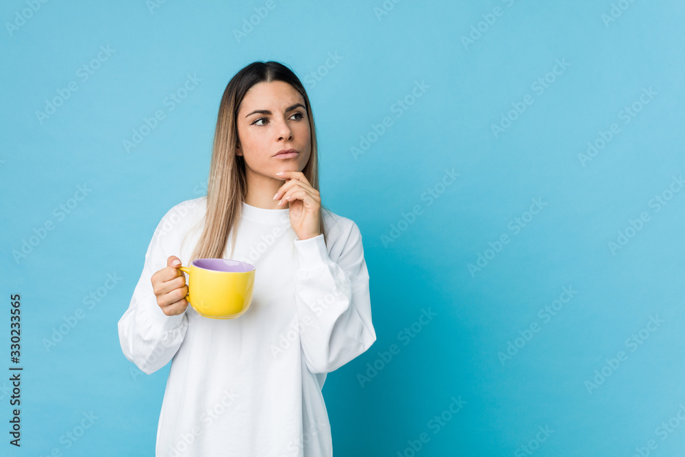 Young caucasian woman holding a coffee cup looking sideways with doubtful and skeptical expression. Young caucasian woman holding a coffee cup looking sideways with doubtful and skeptical expression.