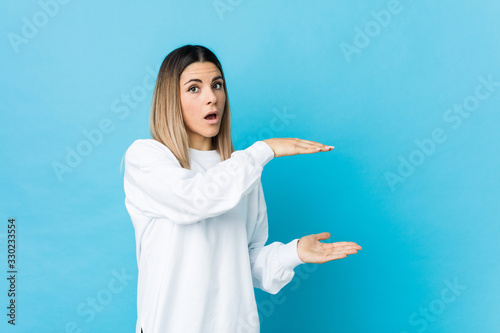 Young caucasian woman isolated shocked and amazed holding a copy space between hands.