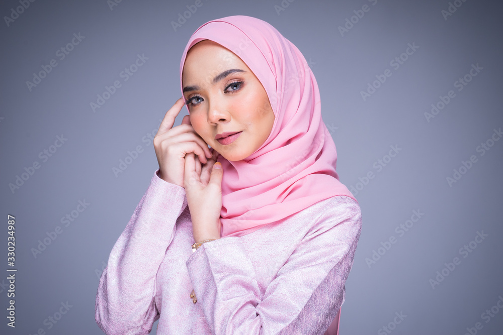 Headshot portrait of a beautiful female model wearing traditional dress and hijab, a lifestyle apparel for Muslim women isolated on grey background. Idul Fitri and hijab fashion concept.