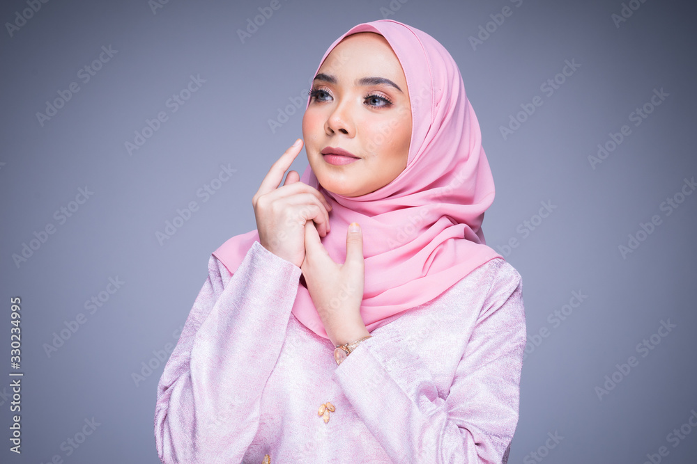 Headshot portrait of a beautiful female model wearing traditional dress and hijab, a lifestyle apparel for Muslim women isolated on grey background. Idul Fitri and hijab fashion concept. Headshot portrait of a beautiful female model wearing traditional dress and hijab, a lifestyle apparel for Muslim women isolated on grey background. Idul Fitri and hijab fashion concept.
