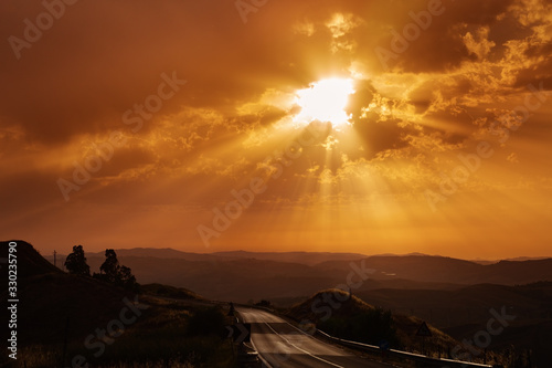 Beautiful landscape with sun and hills at sunrise. Sun rays shine through clouds. Road travel concept. Island Sicily.