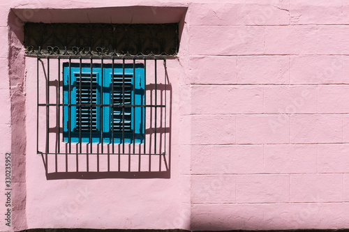Photography Barred window with colonial turquoise blue closed shutters in pink brick exterio