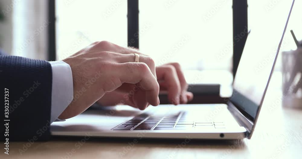 Close up view of male hands using laptop. Businessman wearing suit typing on computer keyboard browsing internet, communicating online, working on modern tech in office. Business software concept.