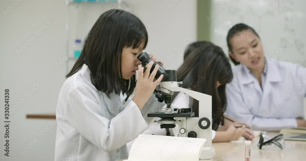 Dolly Shot of Little asian girl attentively looks into microscope on table, Little girl making science experiments in laboratory at school. People with science and education concept. Dolly Shot of Little asian girl attentively looks into microscope on table, Little girl making science experiments in laboratory at school. People with science and education concept.