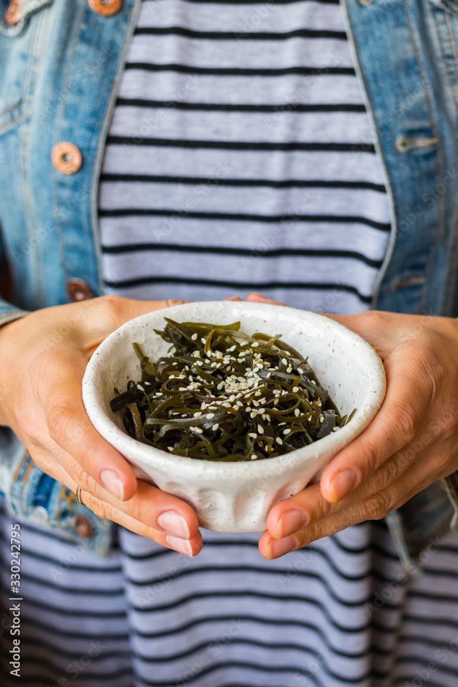 Laminaria kelp seaweed salad with sesame seeds. Woman hands hold Laminaria kelp seaweed salad with sesame seeds. Woman hands hold