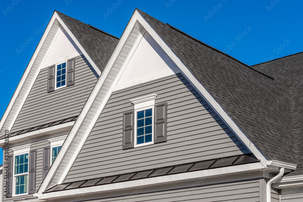 Double gable, with white decorative trim over the windows on a triangle gable roof, white soffit and fascia,  gray horizontal vinyl lap siding with blue sky background