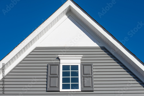 Gable with grey horizontal vinyl lap siding, double hung window with white frame, vinyl shutters on a pitched roof attic at a luxury American single family home neighborhood USA photo