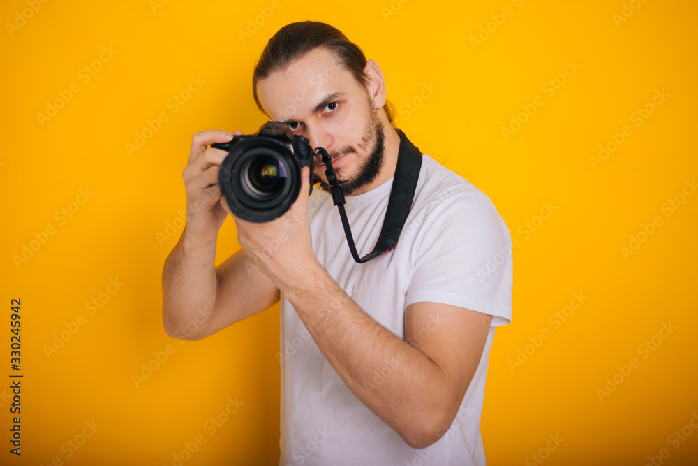 Photographer on a yellow background. The guy is looking into the viewfinder of the camera. Process work. Photographs in the studio Photographer on a yellow background. The guy is looking into the viewfinder of the camera. Process work. Photographs in the studio