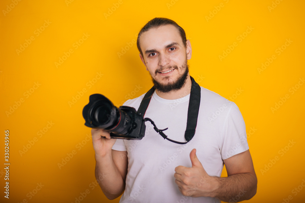 Photographer on a yellow background. The guy is holding a camera. Process work. Photographs in the studio Photographer on a yellow background. The guy is holding a camera. Process work. Photographs in the studio