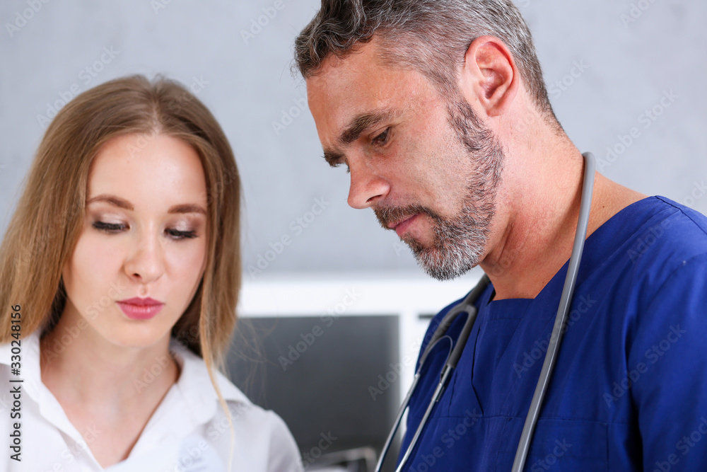 Smiling handsome doctor communicate with patient holding silver pen and showing pad. Physical agreement signature, disease prevention, consent sign, 911, prescribe remedy, healthy lifestyle concept Smiling handsome doctor communicate with patient holding silver pen and showing pad. Physical agreement signature, disease prevention, consent sign, 911, prescribe remedy, healthy lifestyle concept