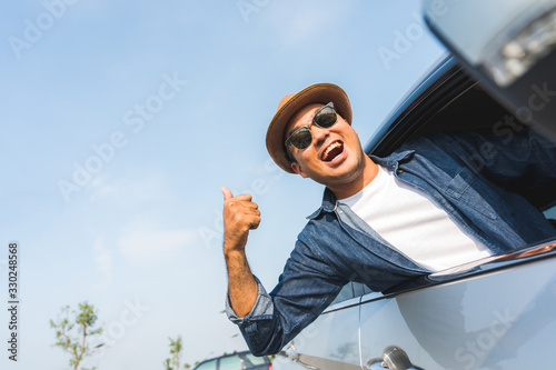 An Asian man is enjoying his trip. He stretches out of the car window to make him look happy.