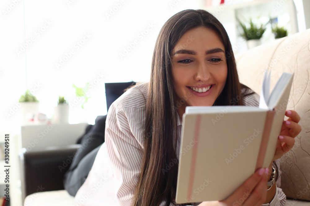 Young attractive indian teenager girl look into open book drink tea lying at couch portrait. Beautiful woman on sofa use datebook synopsis exam preparation delivery concept Young attractive indian teenager girl look into open book drink tea lying at couch portrait. Beautiful woman on sofa use datebook synopsis exam preparation delivery concept