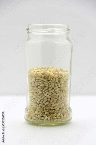 Glass jar with barley on a white background, side view.