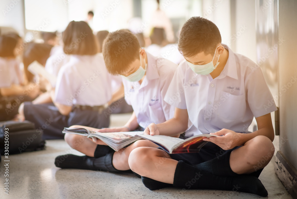 Fototapeta premium The Asian high school students in the white school uniforms wearing the masks and reading the books to prepare final exams in the midst of Coronavirus disease 2019 (COVID-19) epidemic and PM 2.5.