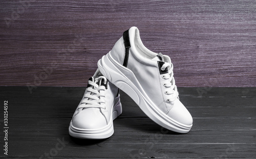 modern leather white sneakers with laces on wooden background