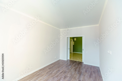 An empty room with white walls and wooden floors . Fresh new renovation. The door to the corridor.