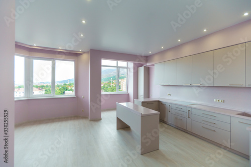 A large room with pink walls and a white kitchen set. Kitchen furniture is new with all kitchen appliances. In front of the kitchen is a white table. Fresh  new renovation.