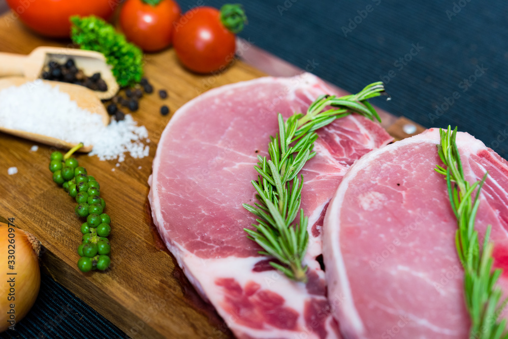 Raw pork chop meat on wood plate with vegetables, spices, salt and black pepper in dark black cloth table