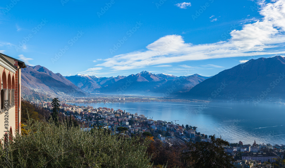 Stunning aerial panorama view of  Locarno cityscape and Lake Maggiore from Madonna del Sasso church, snow covered Swiss Alps mountain and blue sky cloud in background in autumn, Ticino, Switzerland