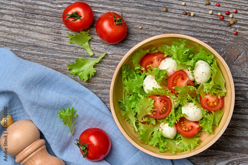 Fresh salad with cherry tomatoes, mozzarella cheese, greens leaves in bowl. Healthy summer salad vegetarian meal concept. Tomatoes and lettuce home made caprese salad on wood, top view Fresh salad with cherry tomatoes, mozzarella cheese, greens leaves in bowl. Healthy summer salad vegetarian meal concept. Tomatoes and lettuce home made caprese salad on wood, top view