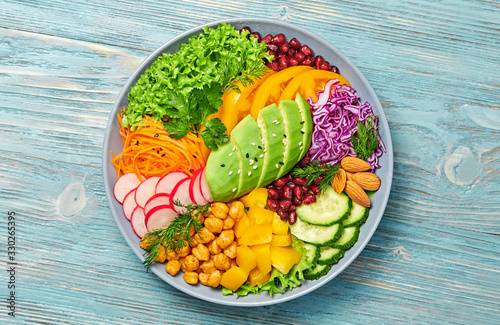 Buddha bowl salad with avocado, tomato, lettuce, cucumber, red cabbage, chickpeas, pomegranate. Vegan and balanced food concept. Fresh rainbow mix green salad on blue wood photo