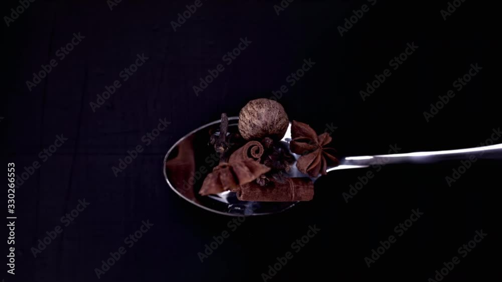 A Full Spoon Of exotic Christmas spice cinnamon anise and nutmeg falling down on black background closeup in super slow motion A Full Spoon Of exotic Christmas spice cinnamon anise and nutmeg falling down on black background closeup in super slow motion